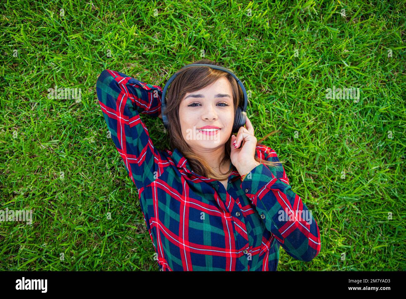 Eine junge Frau hört Musik mit ihren Kopfhörern, die auf einem Rasen liegen Stockfoto