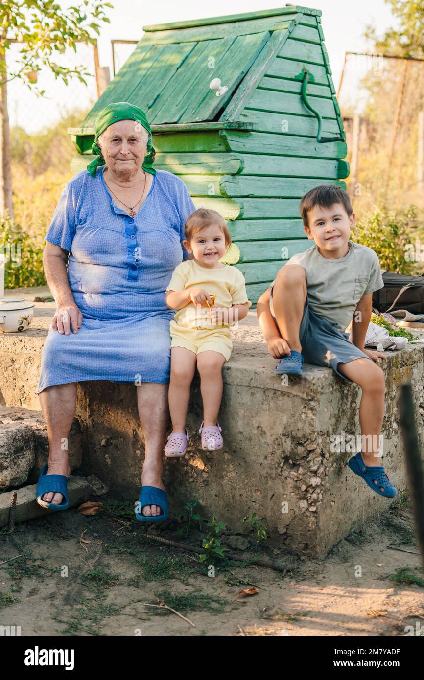 Fröhliche Großmutter, die neben dem Baby-Gig und dem Jungen im Garten sitzt. Garten, Familie und Großeltern. Fürsorge und Glück zusammen. Stockfoto