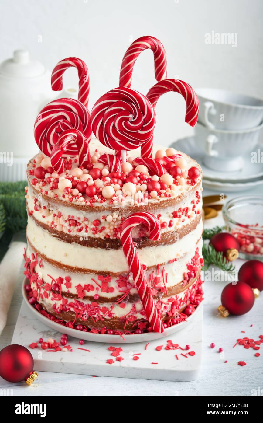 Weihnachten viele Schichten Kuchen dekoriert mit Lolli-Pops, rot-weiße Konfetti auf weißem Kuchenständer, Weihnachtsbälle, Tannenzweige auf weißem Betontisch Stockfoto