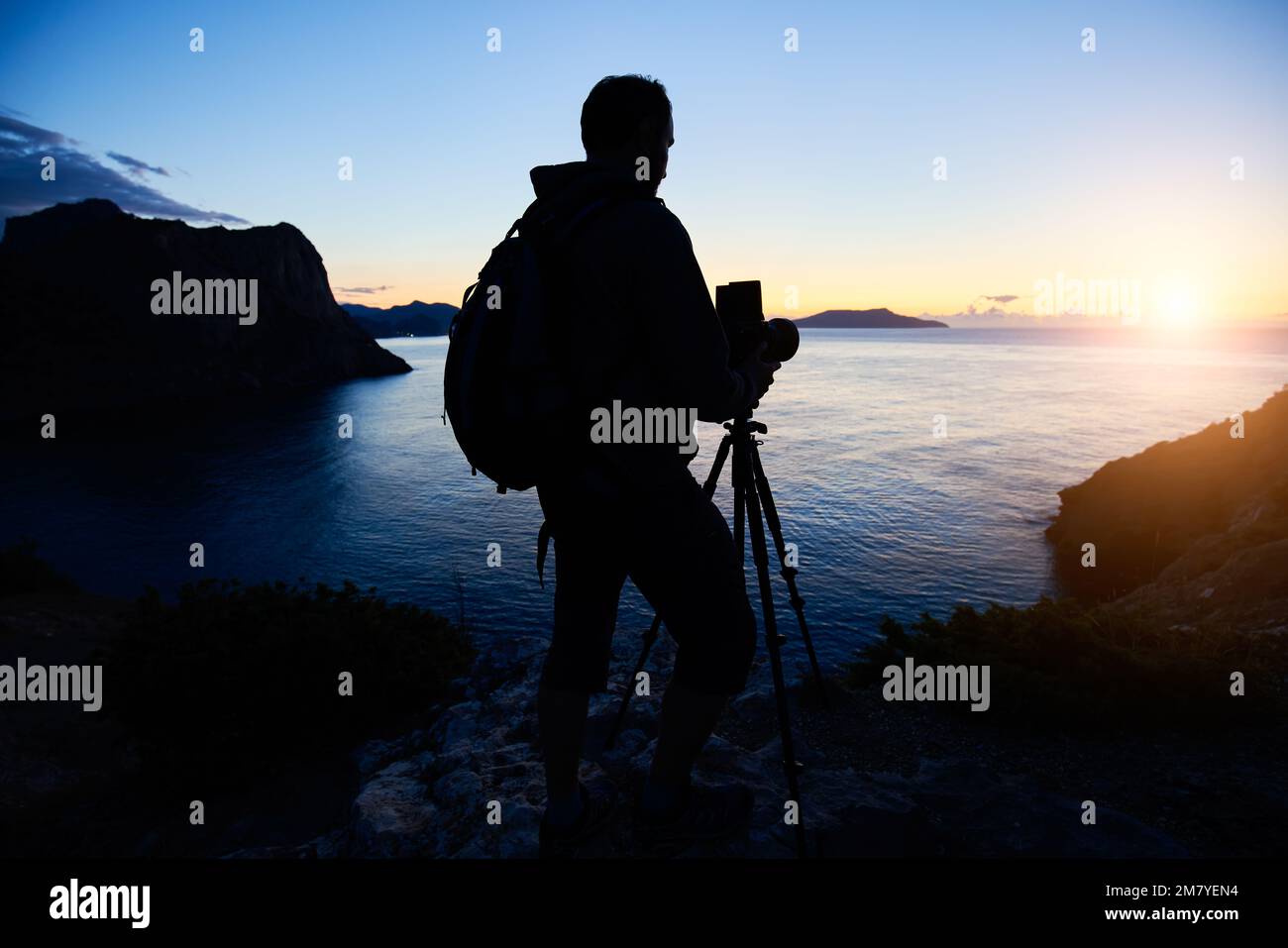 Silhouette des Fotografen auf dem Gipfel des Berges bei Sonnenuntergang. Naturfotograf in Aktion. Analoge Filmfotografie Stockfoto