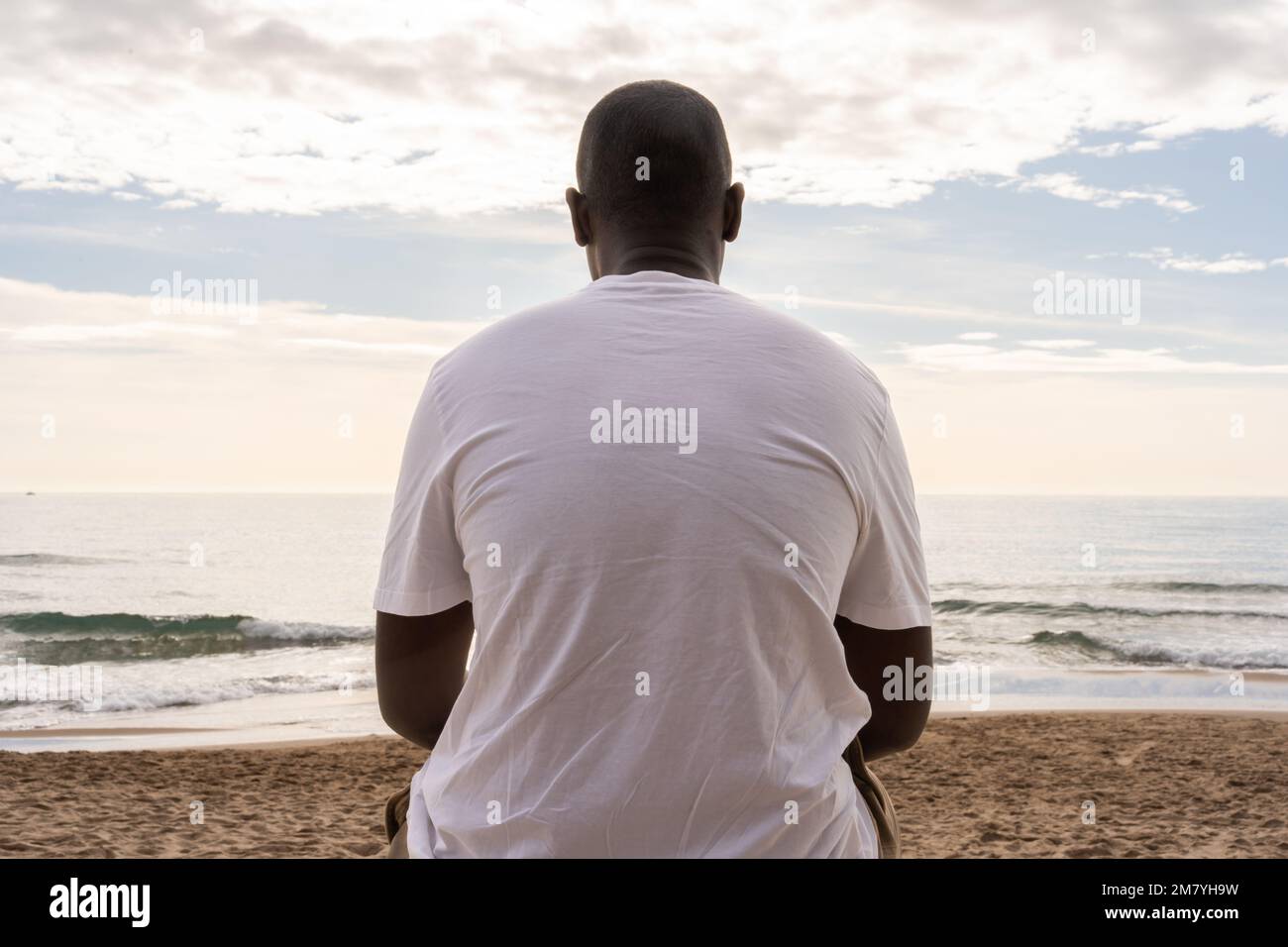 Niedriger Rückblick auf einen nicht wiedererkennbaren afroamerikanischen Mann in legerem, weißem T-Shirt am Sandstrand und bestaunen das winklige Meer Stockfoto