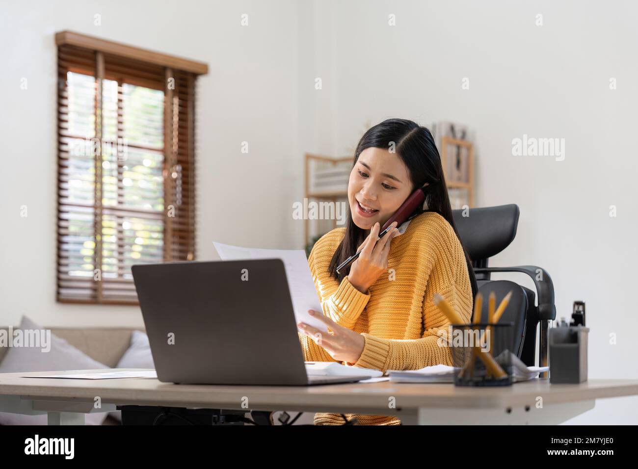 Asiatische Frau, die telefoniert und mit einem Laptop-Taschenrechner auf einem Büroschreibtisch arbeitet, plant die Analyse des Finanzberichts, Geschäftsplan Stockfoto