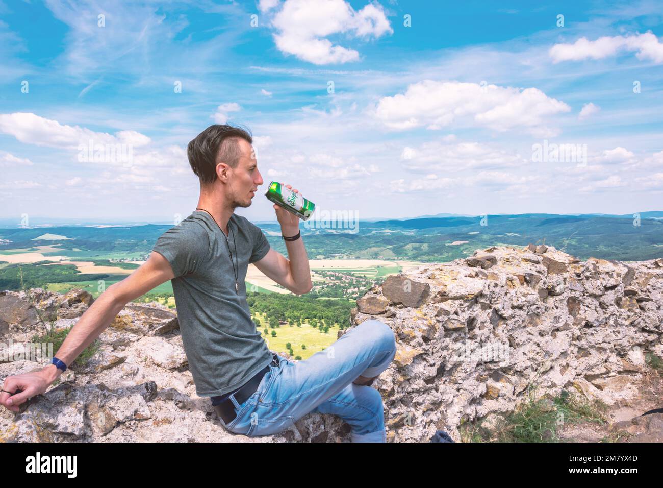 Ein Mann ruht auf den Überresten einer Burgmauer, während er Bier trinkt, Szanda, Ungarn Stockfoto
