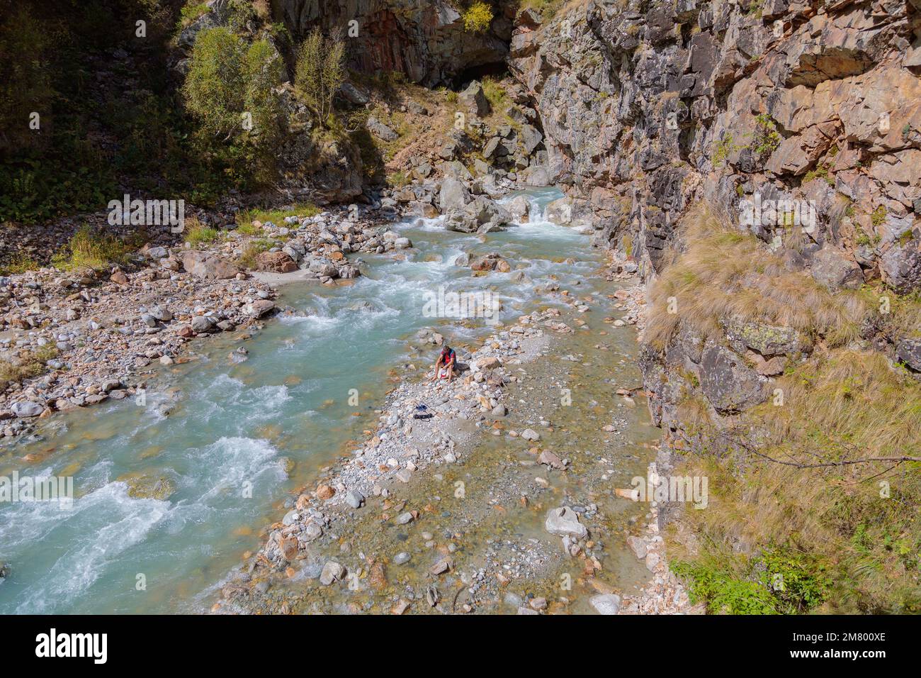 Ein männlicher Tourist sitzt am Fluss in den Bergen. Wandern in den Bergen. Stockfoto