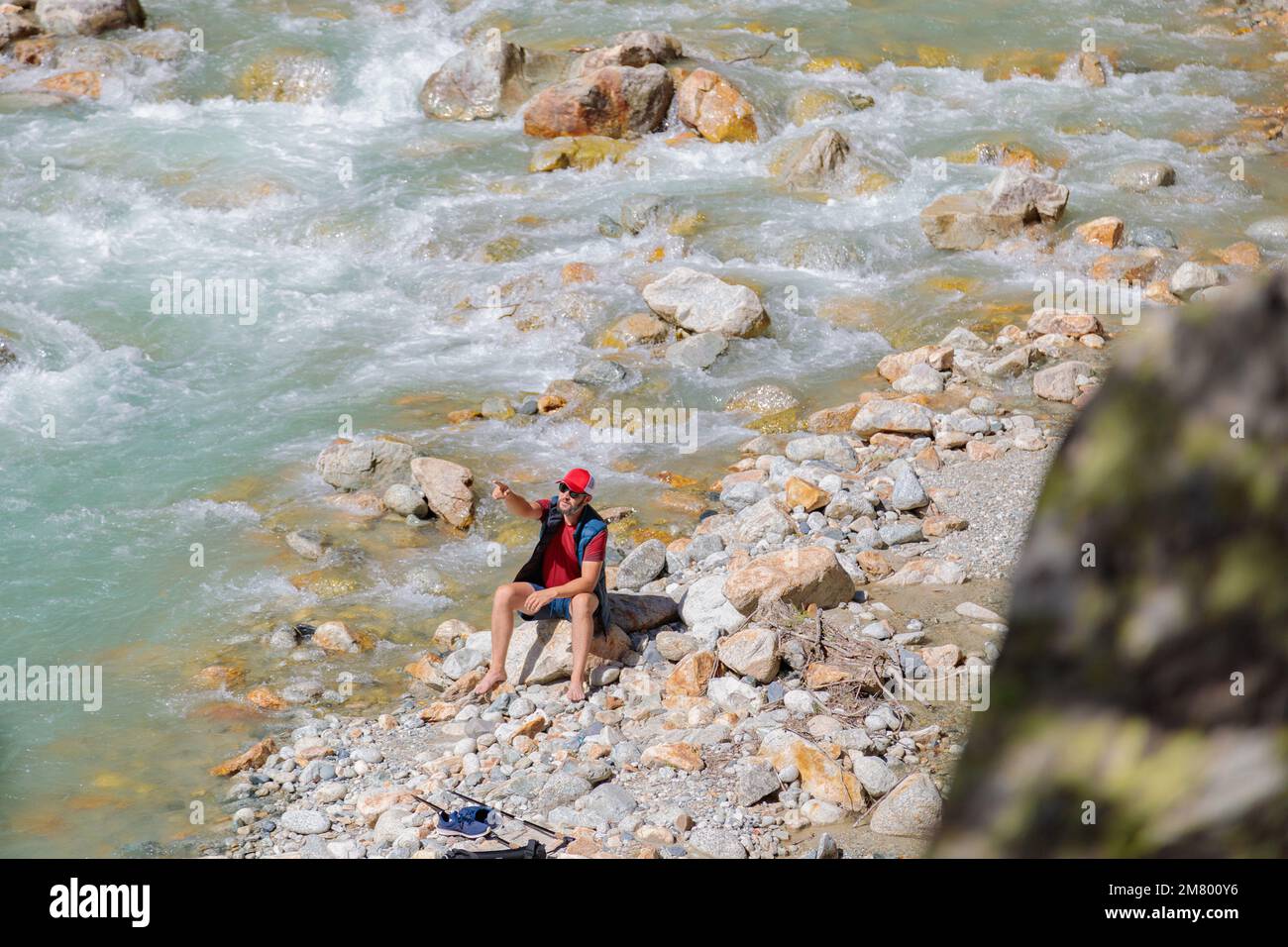 Ein männlicher Tourist sitzt am Fluss in den Bergen. Wandern in den Bergen. Stockfoto