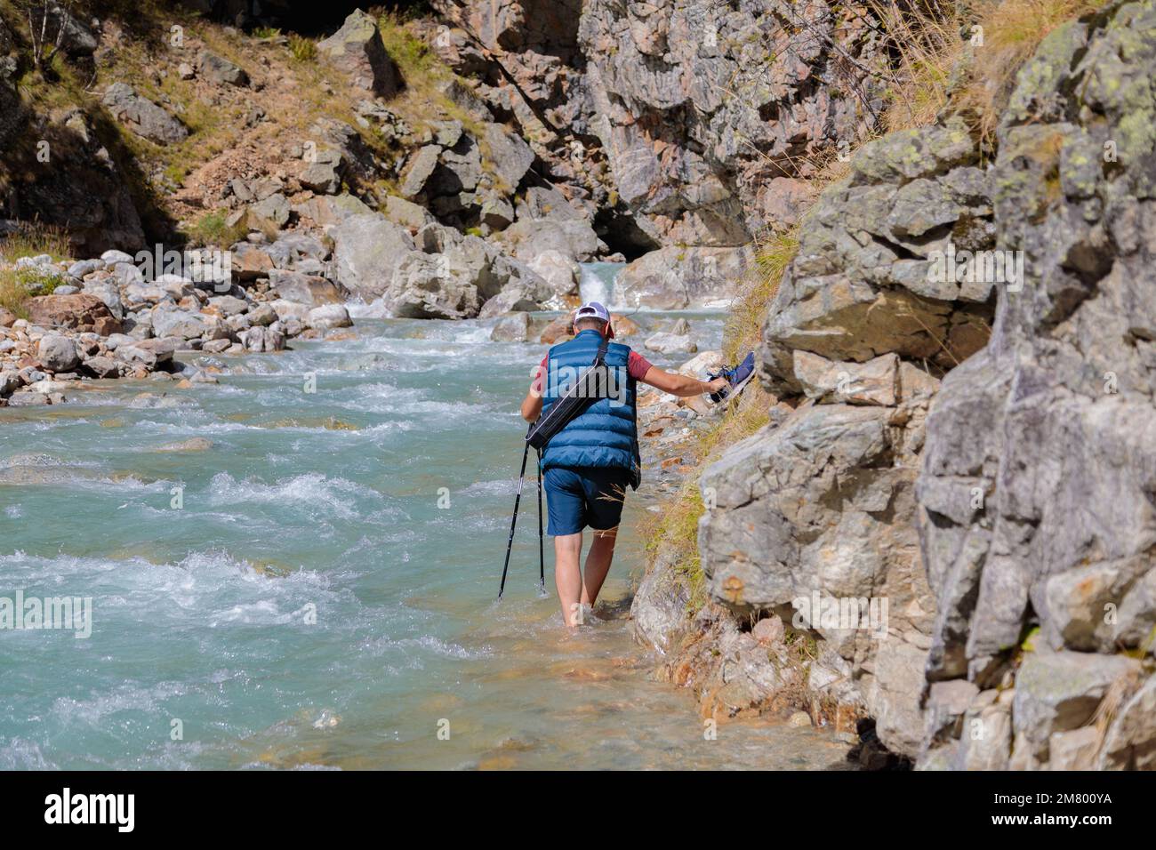 Ein männlicher Tourist fährt am Fuße eines Flusses in den Bergen vorbei. Wandern in den Bergen. Stockfoto