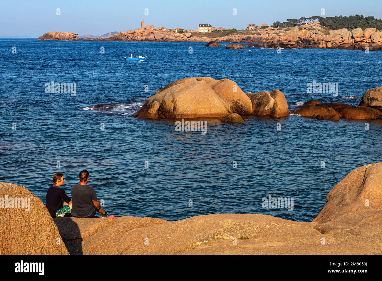 EIN PAAR MIT BLICK AUF DIE ROSAFARBENEN GRANITFELSEN DES LEUCHTTURMS PLOUMANACH BEI SONNENUNTERGANG, RENOTE ISLAND POINT, TREGASTEL, DIE ROSAFARBENE GRANITKÜSTE, COTES-D’ARMOR, BRITTANY, FRANKREICH Stockfoto