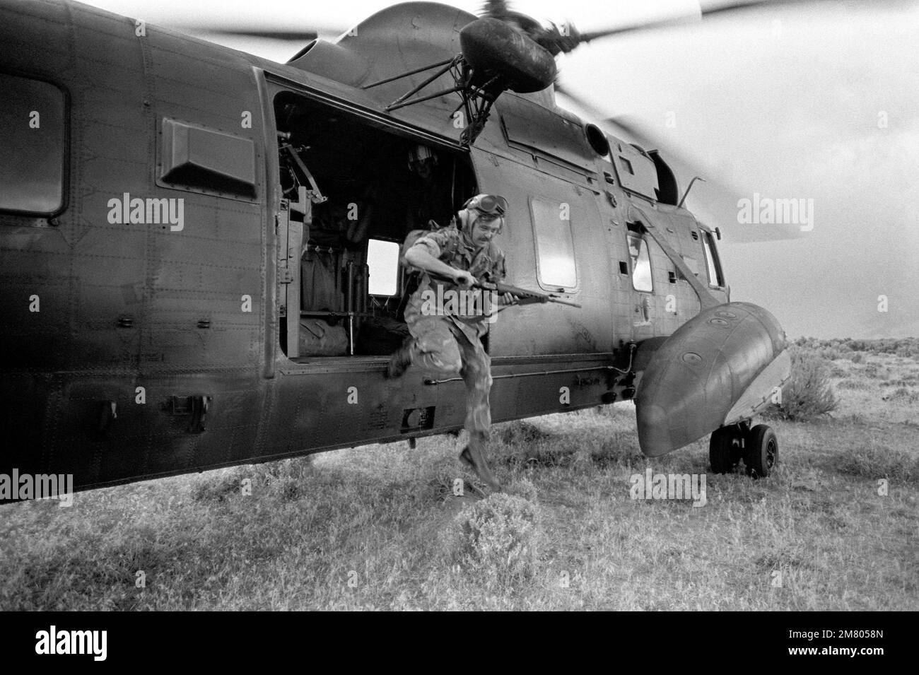 Ein Special Warfare Crewman der US Navy (USN) trägt ein 5,56 mm M16A1-Gewehr, wenn er einen USN Sikorsky SH-3 Sea King Helicopter verlässt, während er an einer Kampfübung zur Such- und Rettungsaktion (SAR) am Luftwaffenstützpunkt Mountain Home (AFB), Idaho (ID) teilnimmt. Basis: Mountain Home Luftwaffenstützpunkt Staat: Idaho (ID) Land: Vereinigte Staaten von Amerika (USA) Stockfoto