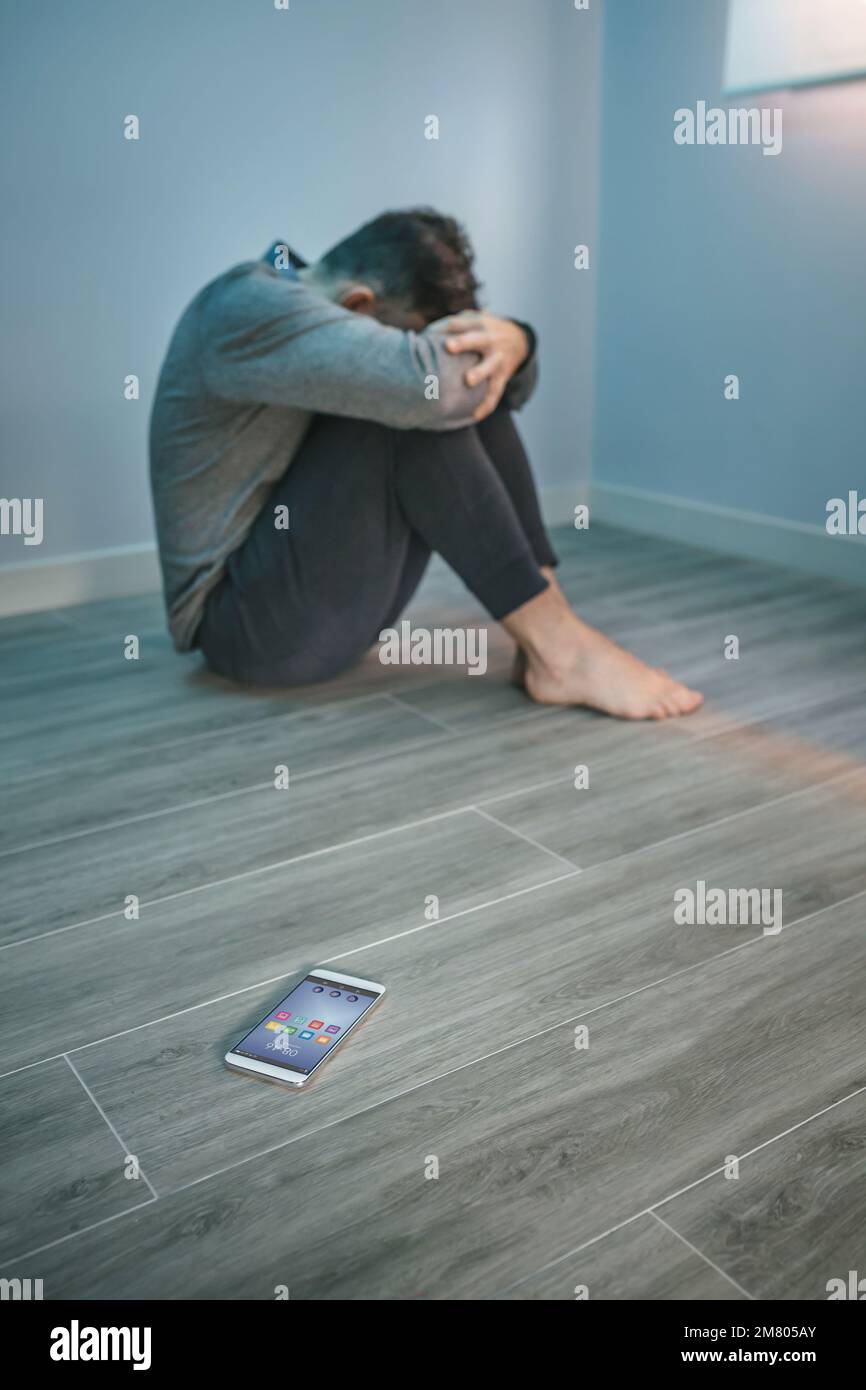 Mann mit Problemen, der auf dem Boden saß und ein Handy auf dem Boden hatte Stockfoto