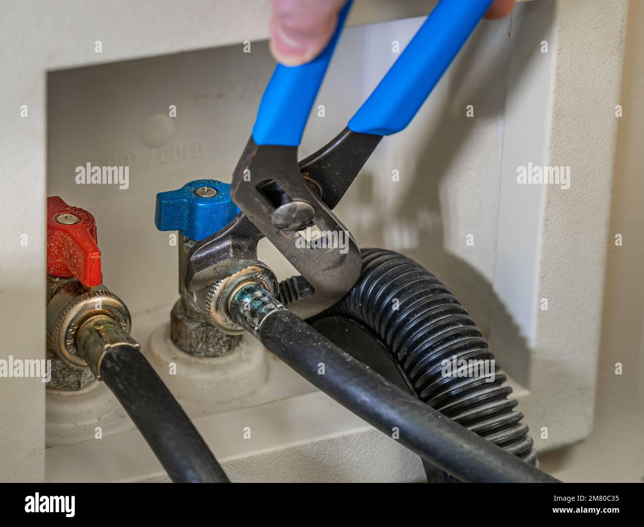 Mit einem Schraubenschlüssel die Wasserversorgungsleitung am Absperrventil der Wäschewaschmaschine befestigen. Stockfoto