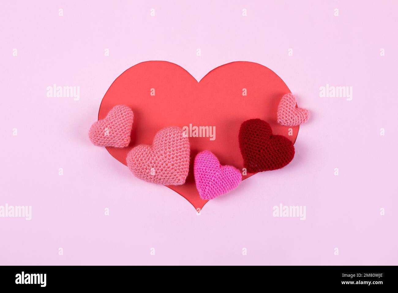 Gekräuselte rosa und burgunderrote Herzen auf rosa Hintergrund in Herzform. Valentinstag, Symbol der Liebe. Stockfoto