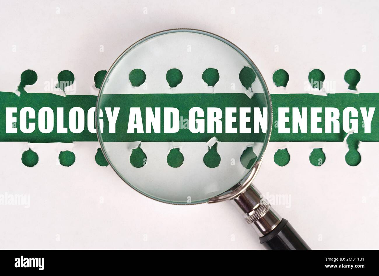 Zwischen zwei Blättern eines Notizbuchs auf einem grünen Streifen mit der Aufschrift „Ecology“ und „Green Energy“ befindet sich eine Lupe. Das Konzept ist "Ecolo" Stockfoto