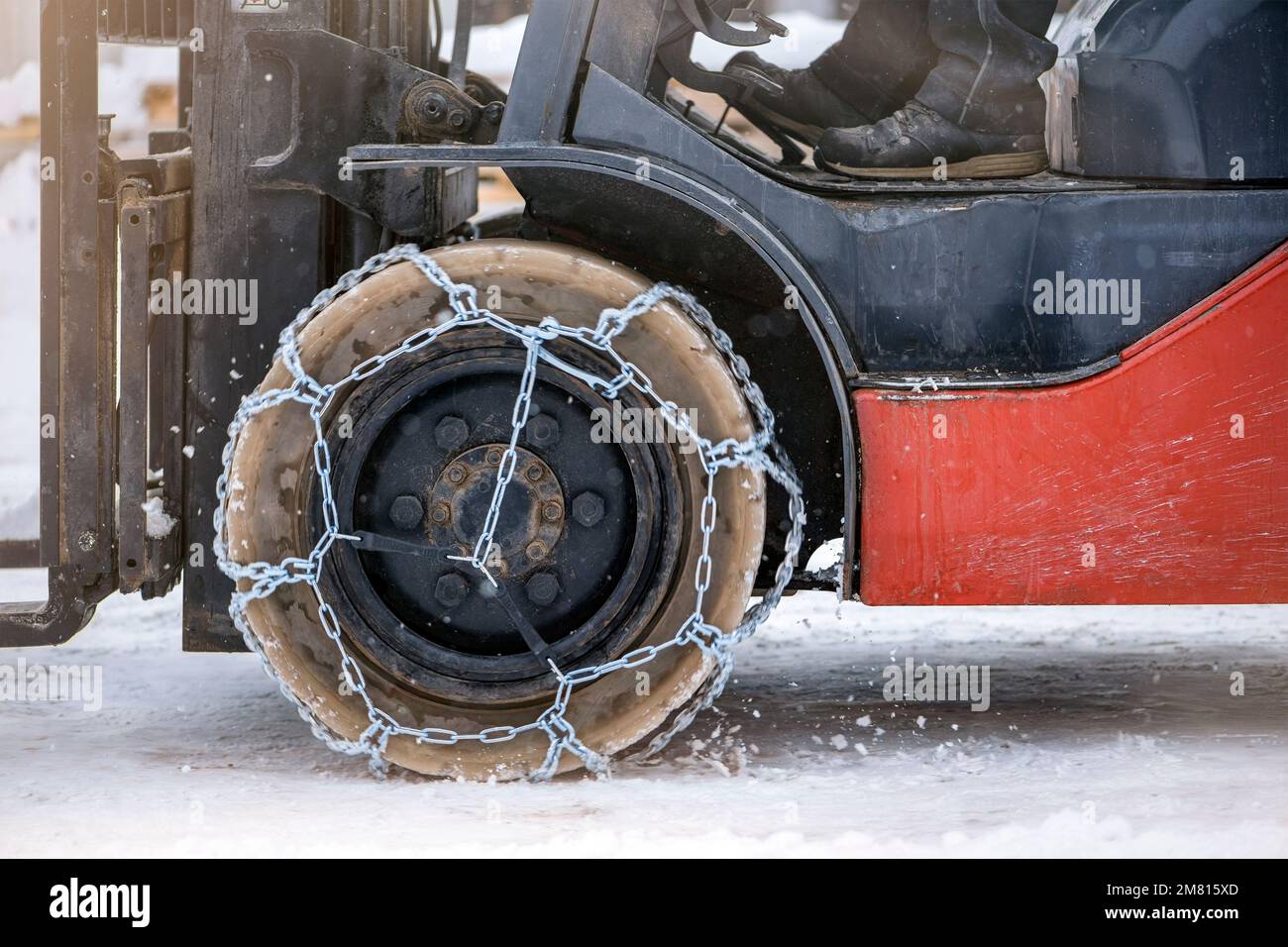 Traktorrad mit Kette. Traktor oder Lader auf einer rutschigen, verschneiten Straße. Lader fahren mit rutschfesten Ketten auf Schnee. Stockfoto