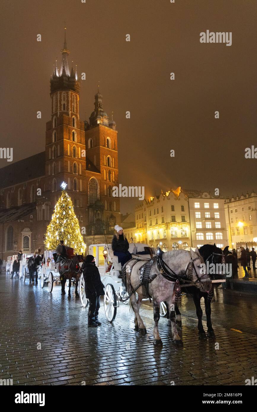 Reisen Sie nach Krakau; Hauptmarktplatz bei Nacht, mit beleuchteter St. Marys Kirche und Pferd und Kutsche zu Weihnachten für den Weihnachtsmarkt, Krakau Polen Stockfoto