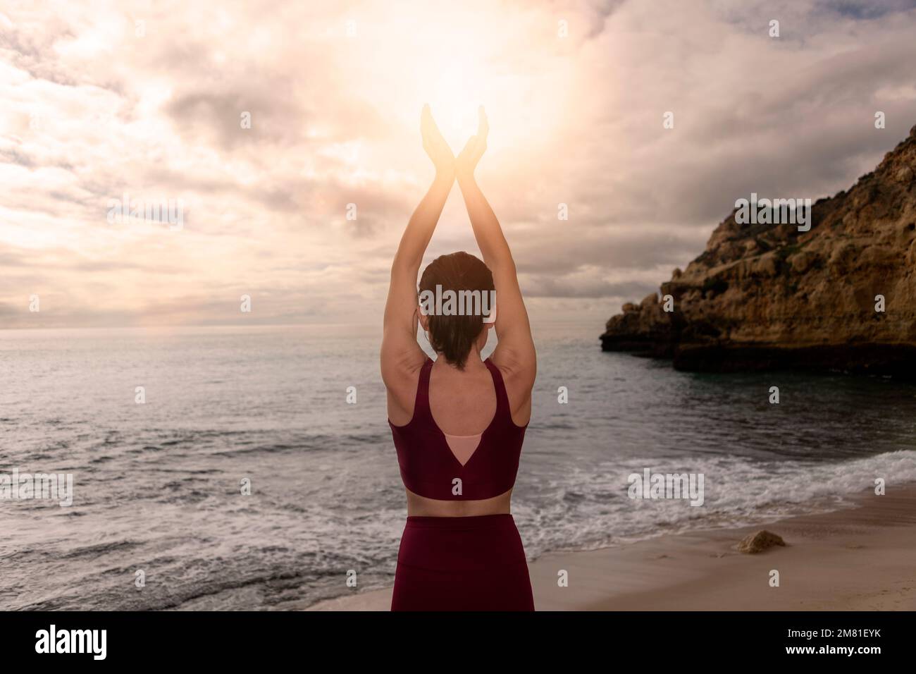 Rückansicht einer Frau, die meditiert und die Sonne am Meer in ihre Hände steckt. Stockfoto