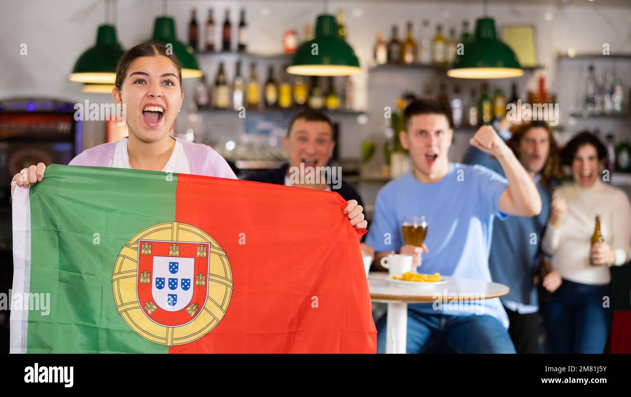 Gesellschaft von schreienden jungen erwachsenen Sportfans, die die Flagge Portugals schwenken und die Nationalmannschaft mit Bier im Pub unterstützen Stockfoto