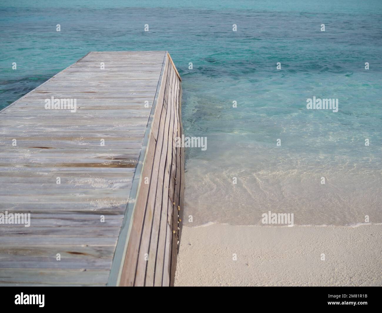 Verwitterter Holzpier, der in das kristallklare Wasser des Indischen Ozeans neben weißem Sand auf einer maledivischen Insel ragt Stockfoto