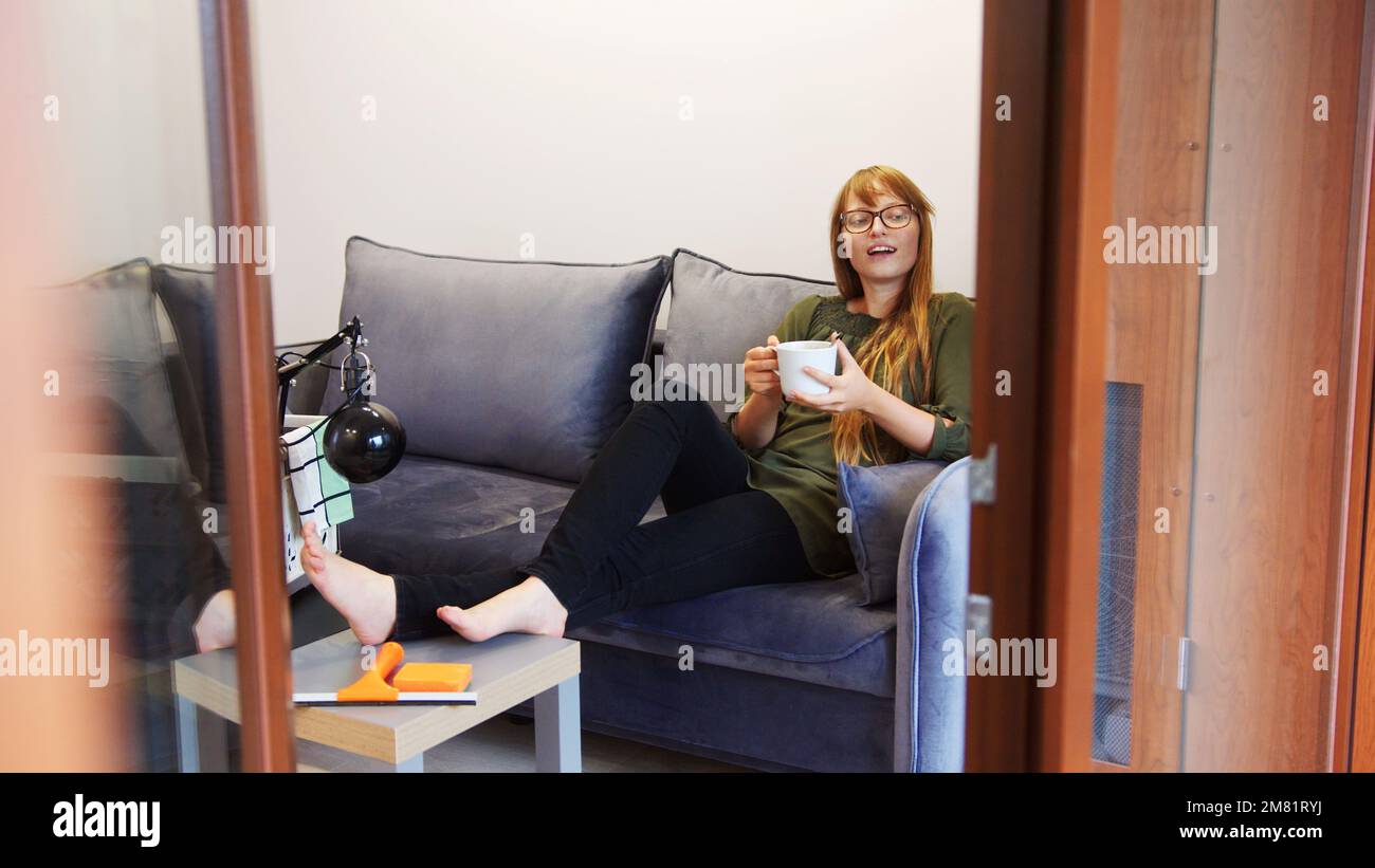 Junge weiße Frau, die sich mit einer Tasse Tee auf der Couch entspannt. Hochwertiges Foto Stockfoto