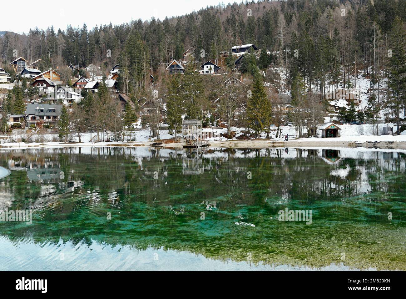 Das klare Wasser der ruhigen Jasna-Seen im Triglav-Nationalpark in Slowenien spiegelt die umliegenden alpinen Chalets wider Stockfoto