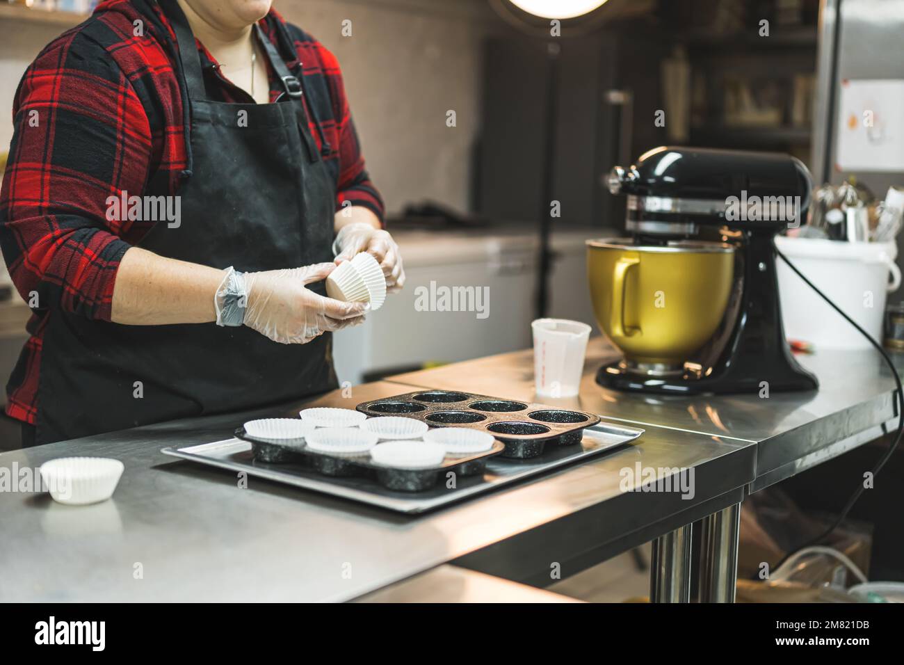 Unbekannte Person in schwarzem Schürzenfutter Papier Cupcake Formen in Muffin-Futter. Professionelle Bäckerei Küche Interieur. Hochwertiges Foto Stockfoto