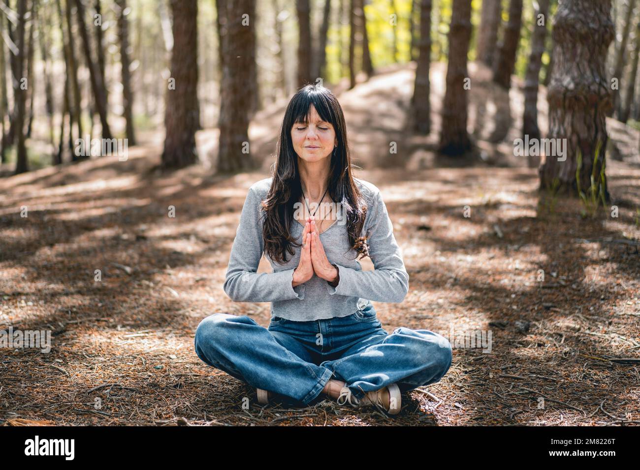 Vorderansicht einer Frau, die sich im Wald die Hände zusammenschlägt. Namaste-Pose. Stockfoto