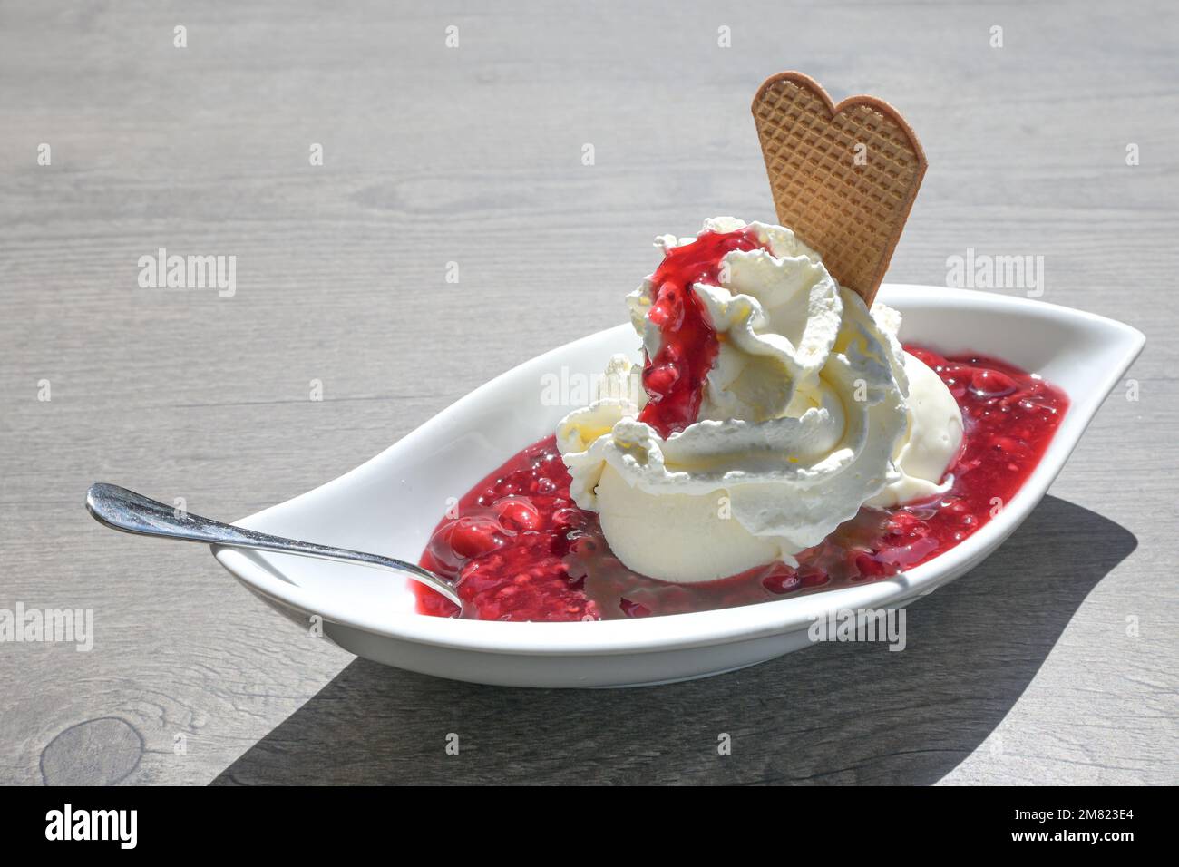 Vanilleeis mit Schlagsahne und rotem Gruetze, eine rote Fruchtgelee aus Deutschland und Dänemark, Sommerdessert in einer weißen Schüssel auf einem grauen Tisch, Polizist Stockfoto