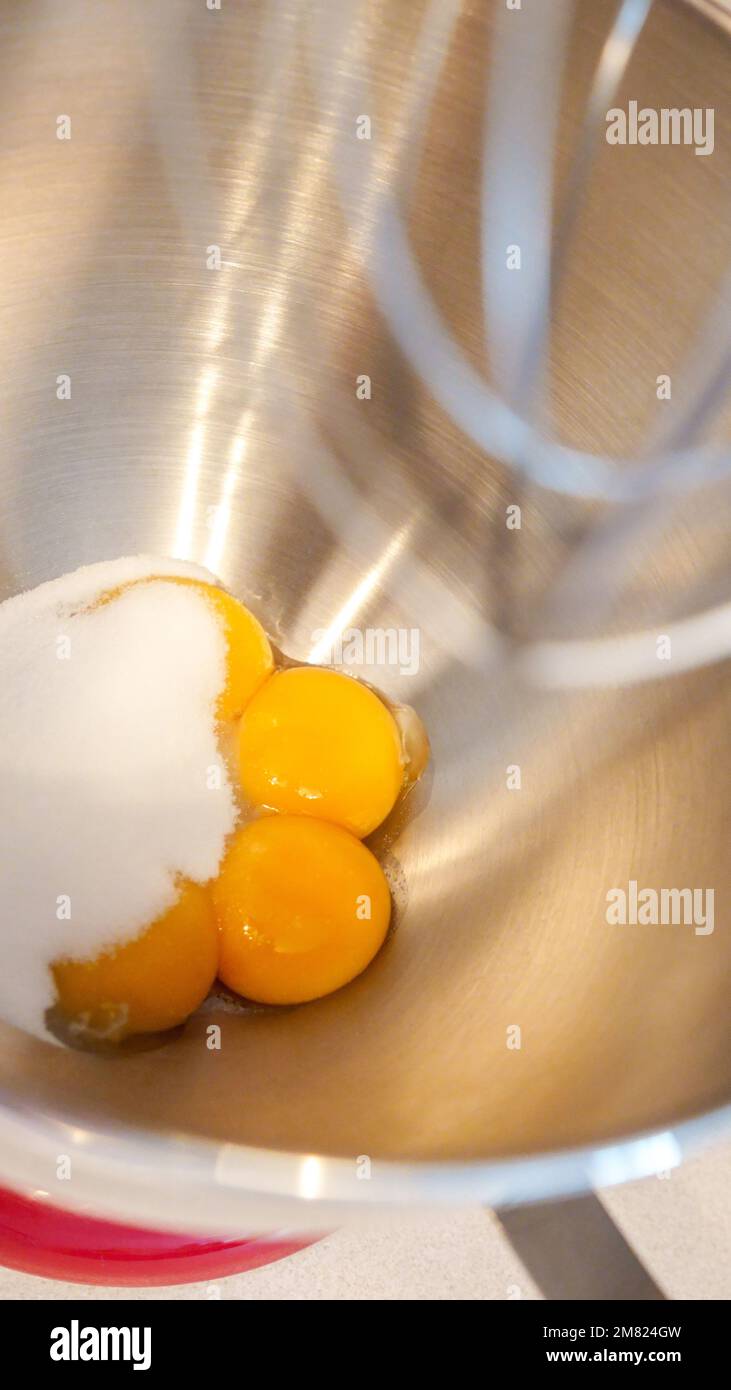 Rohe Eier in einer Metallschüssel mit stehendem Mixer. Eigelb mit Zucker in der Küchenarmatur zubereiten Stockfoto