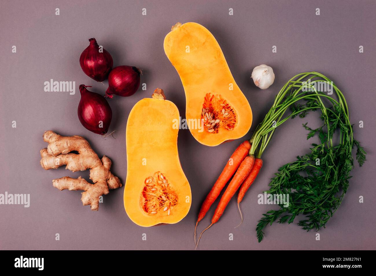 Roher Butternusskürbis mit Karotten, roten Zwiebeln, Ingwer und Knoblauch auf grauem Hintergrund. Zutaten für Kürbissuppe. Draufsicht, flach liegend. Stockfoto