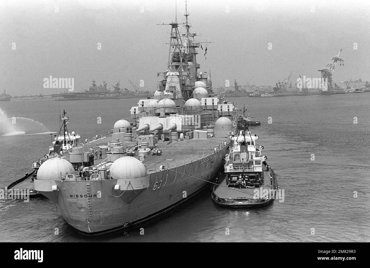 Der große Hafenschlepper USS SACO (YTB 796) und mehrere Schlepper ziehen das Schlachtschiff MISSOURI (BB 63) zur Long Beach Naval Shipyard, wo es reaktiviert/modernisiert wird. Beachten Sie die „Iglus“, die zum Schutz der 40-mm-Pistolenhalterungen verwendet wurden, während das Schiff in Reserve war. Im Hintergrund sind die USS NEW JERSEY (BB 62) und die USS PELELIU (LHA 5) zu sehen. Basis: Long Beach Bundesstaat: Kalifornien (CA) Land: Vereinigte Staaten von Amerika (USA) Stockfoto