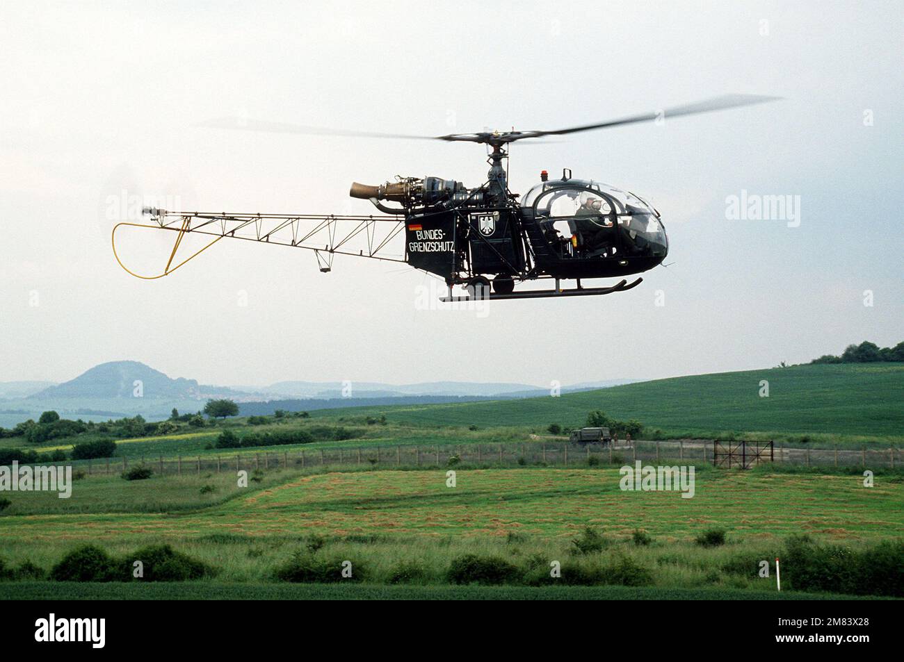 Eine rechte Seitenansicht eines westdeutschen Alouette-III-Hubschraubers, der die ostdeutsche Grenze patrouilliert. Die ostdeutschen Grenzschutzbeamten sind im Hintergrund. Basis: Kassel Land: Bundesrepublik Deutschland (BRD) Stockfoto
