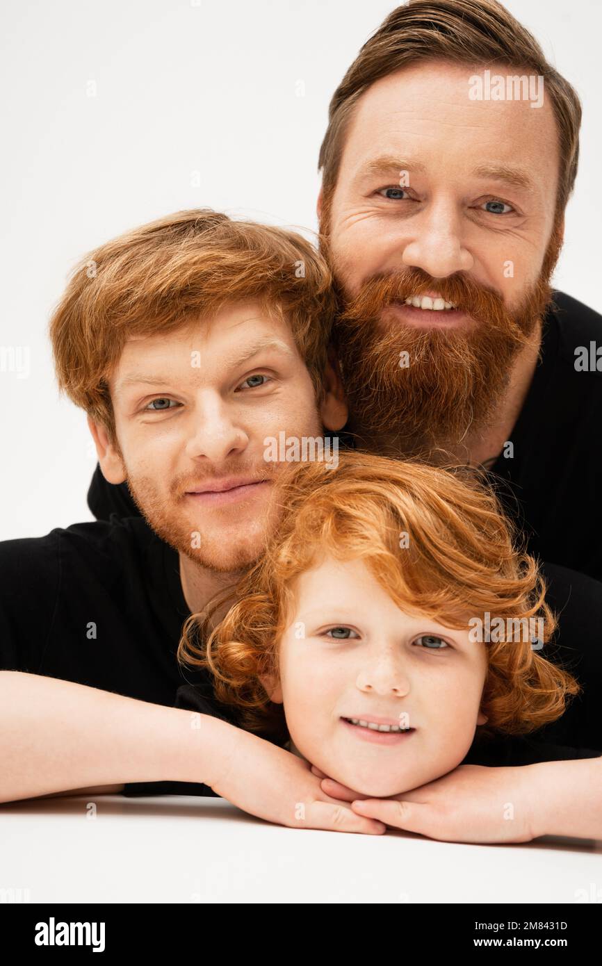 Familienporträt eines rothaarigen Kindes mit Vater und bärtigem Großvater, der vor der Kamera lächelt, auf hellgrauem Hintergrund, Stockbild Stockfoto