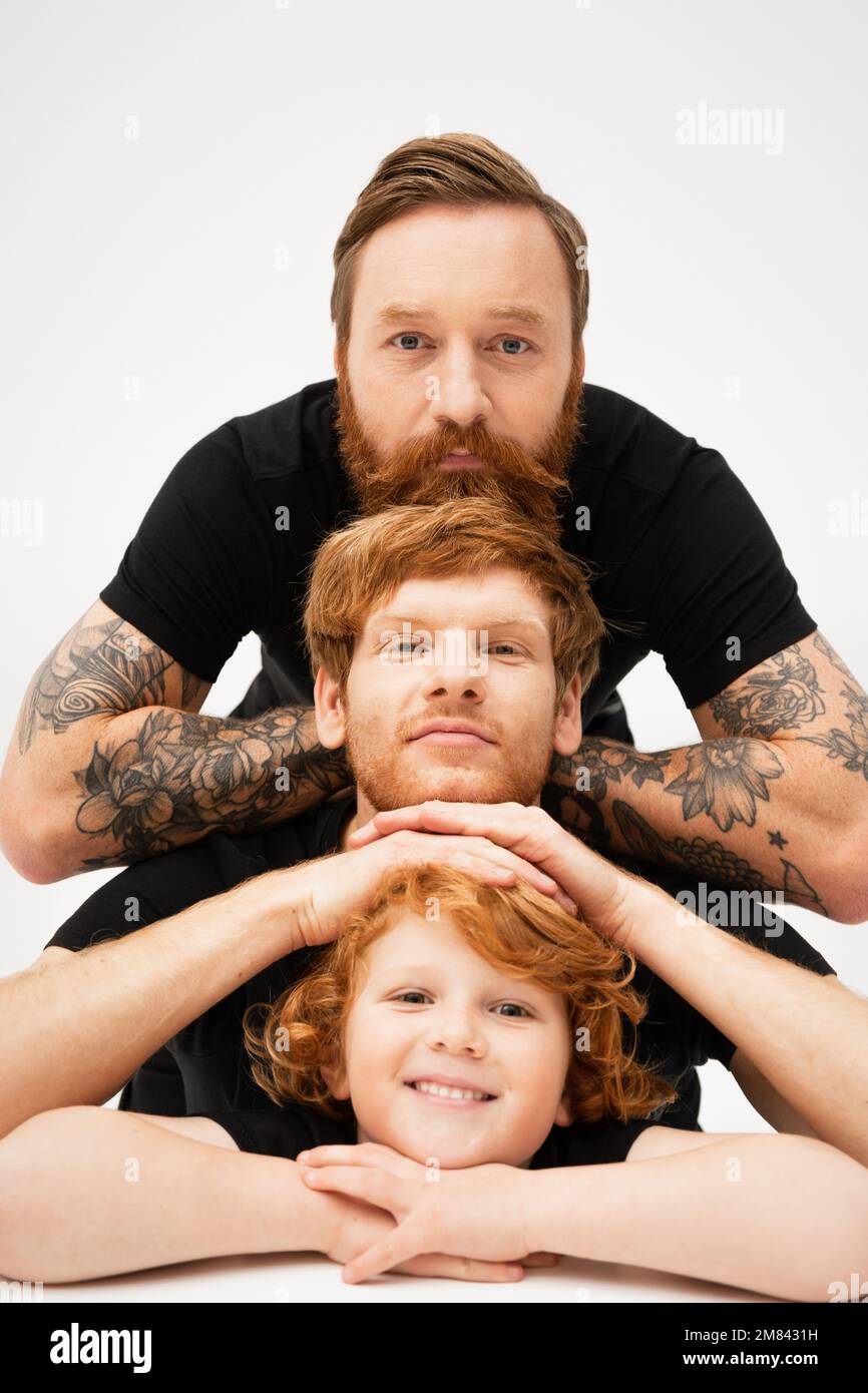 Familienporträt eines bärtigen tätowierten Mannes mit rothaarigem Sohn und Enkel auf hellgrauem Hintergrund, Stockbild Stockfoto