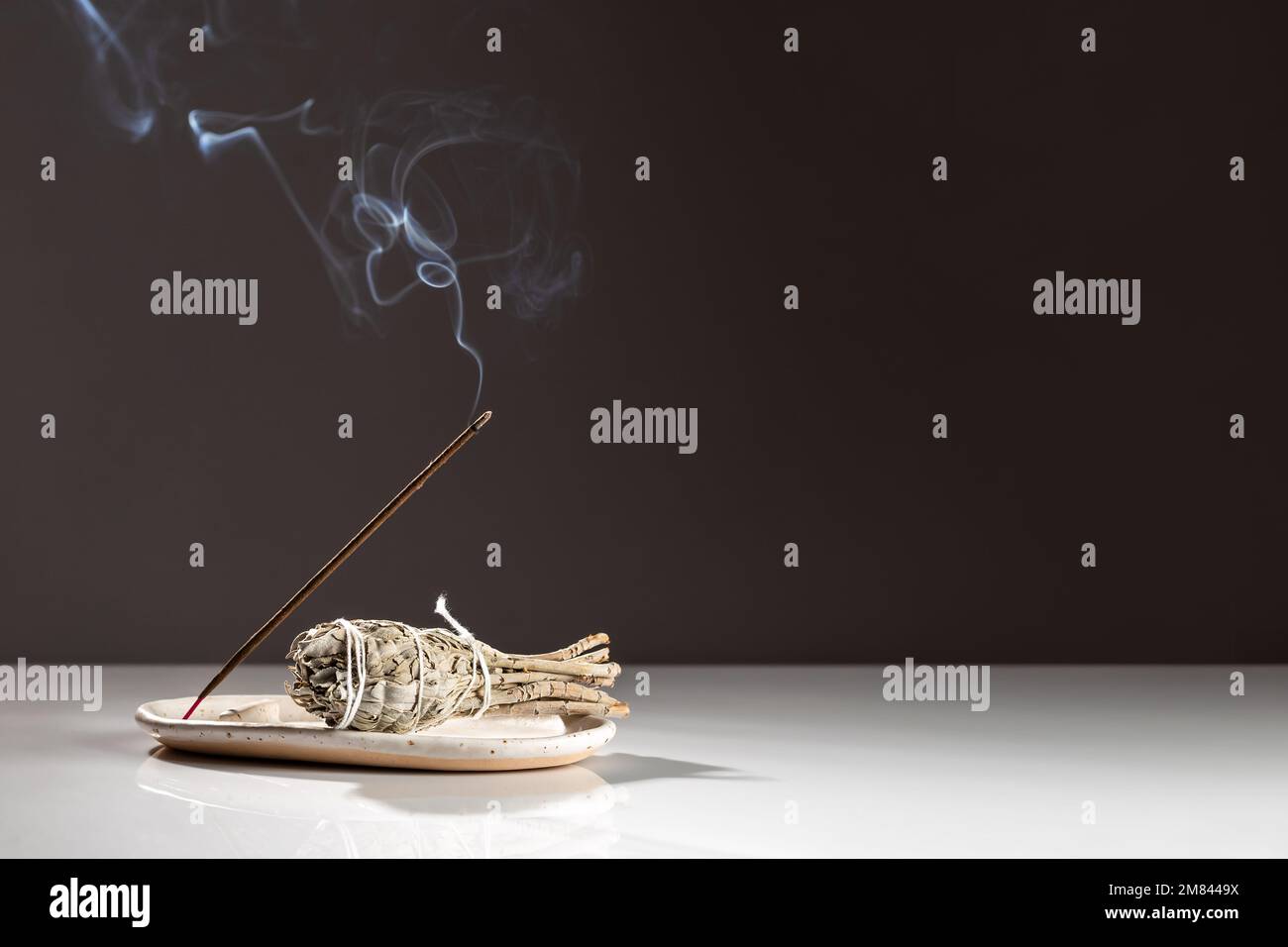 Brennender aromatischer Incense Smoky Stick und ein Bündel Salvia Salvia Salbe auf weißem Tablett auf dunklem minimalistischem Hintergrund. Aromatherapie-Rauch für Meditation und Re Stockfoto