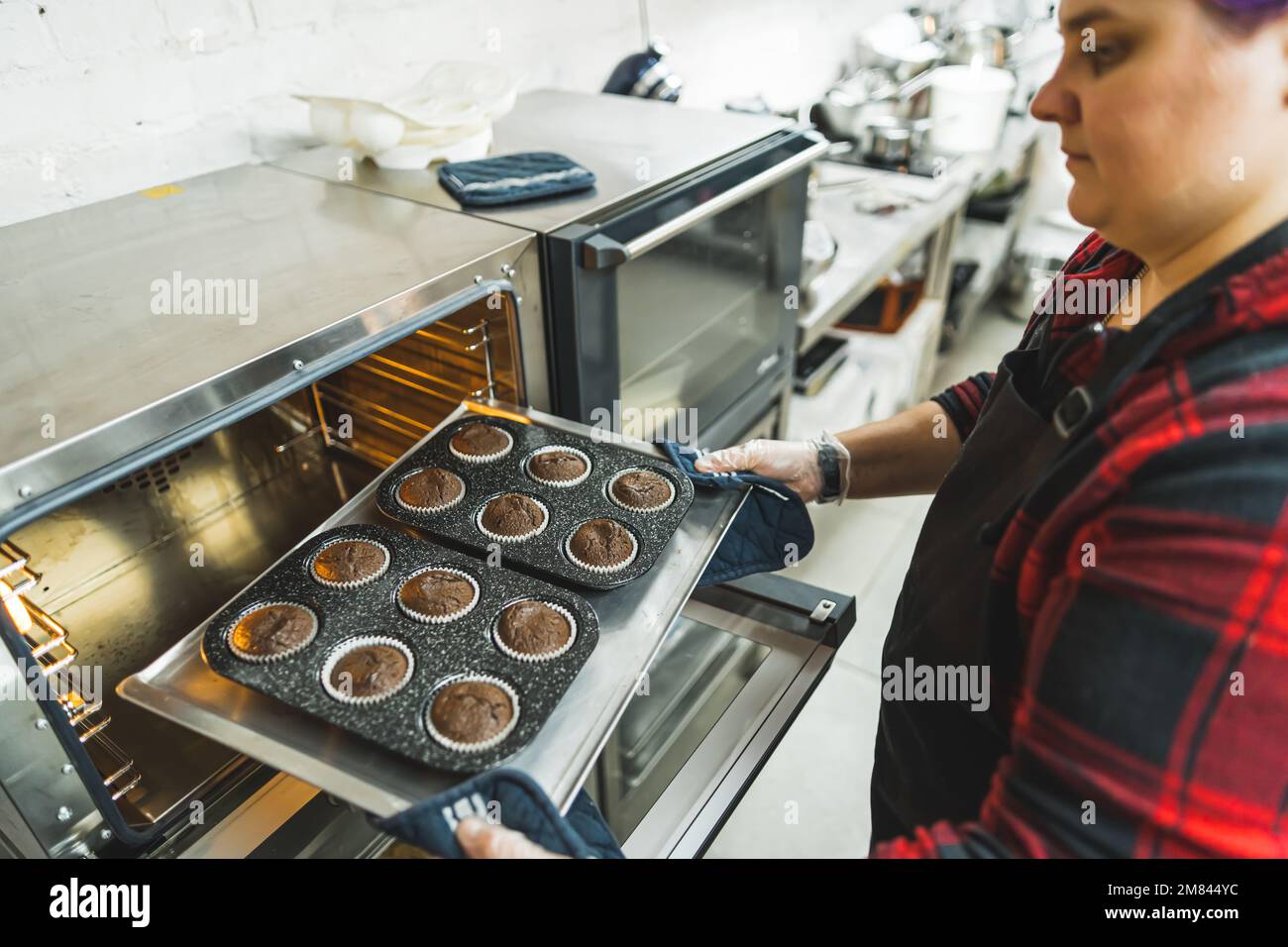 Die Chefköchin nimmt Schokoladen-Muffins aus dem Ofen und bereitet Süßigkeiten zu. Hochwertiges Foto Stockfoto