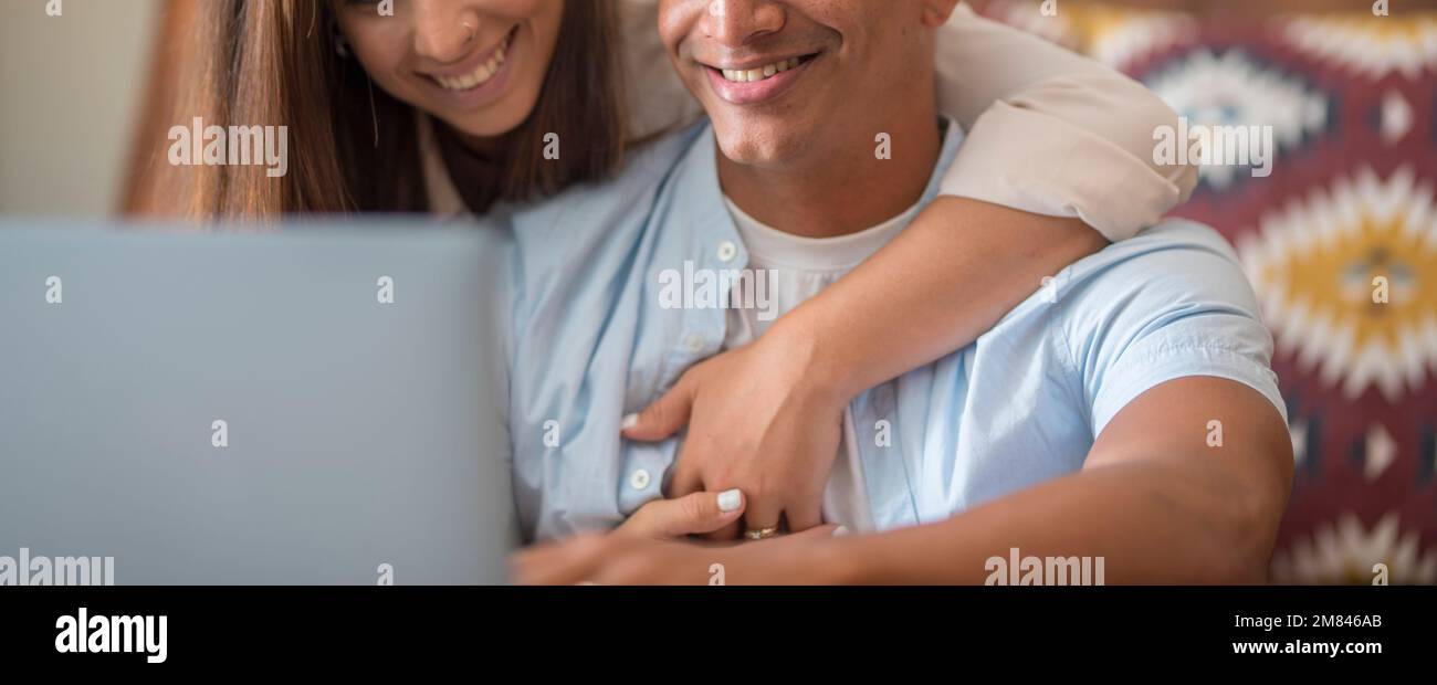 Bannerbild eines schwarz-weißen Mannes und einer weißen Frau, die glücklich mit einem Notebook zu Hause arbeiten und sich mit Liebe und Beziehung umarmen. Ein junges Paar lebt Stockfoto