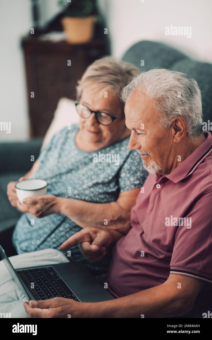 Alte Leute, die zu Hause Computer benutzen. Ältere Männer und Frauen surfen im Internet über eine drahtlose Laptop-Verbindung. Moderne Rentner, die ihre Aufmerksamkeit genießen Stockfoto