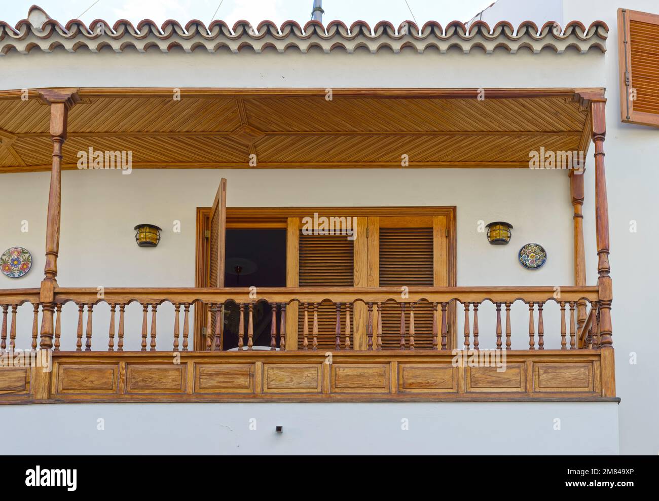 Vergrößerung des Balkons mit Holzdach, Geländer und horizontaler Sonnenblende an Tür- und Fensterläden. Stockfoto