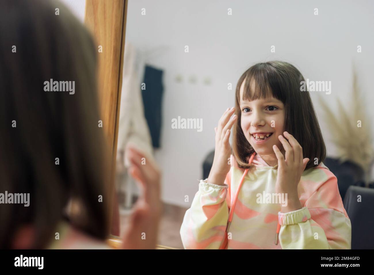 Mädchen mit neuer Frisur im Friseursalon, die sich selbst in einen Spiegel guckt. Sie hat einen Pony. Stockfoto