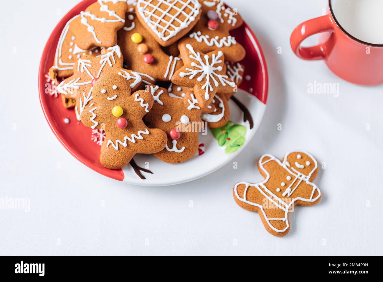 Lebkuchen-Kekse in Form eines Ingwermanns auf rotem Teller. Weißer Hintergrund. Traditionelles Weihnachtsdessert. Verspielt und glücklich. Stockfoto