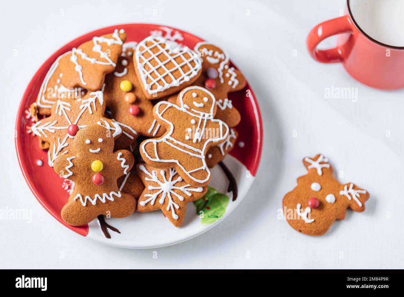 Lebkuchen-Kekse in Form eines Ingwermanns auf rotem Teller. Weißer Hintergrund. Traditionelles Weihnachtsdessert. Verspielt und glücklich. Stockfoto