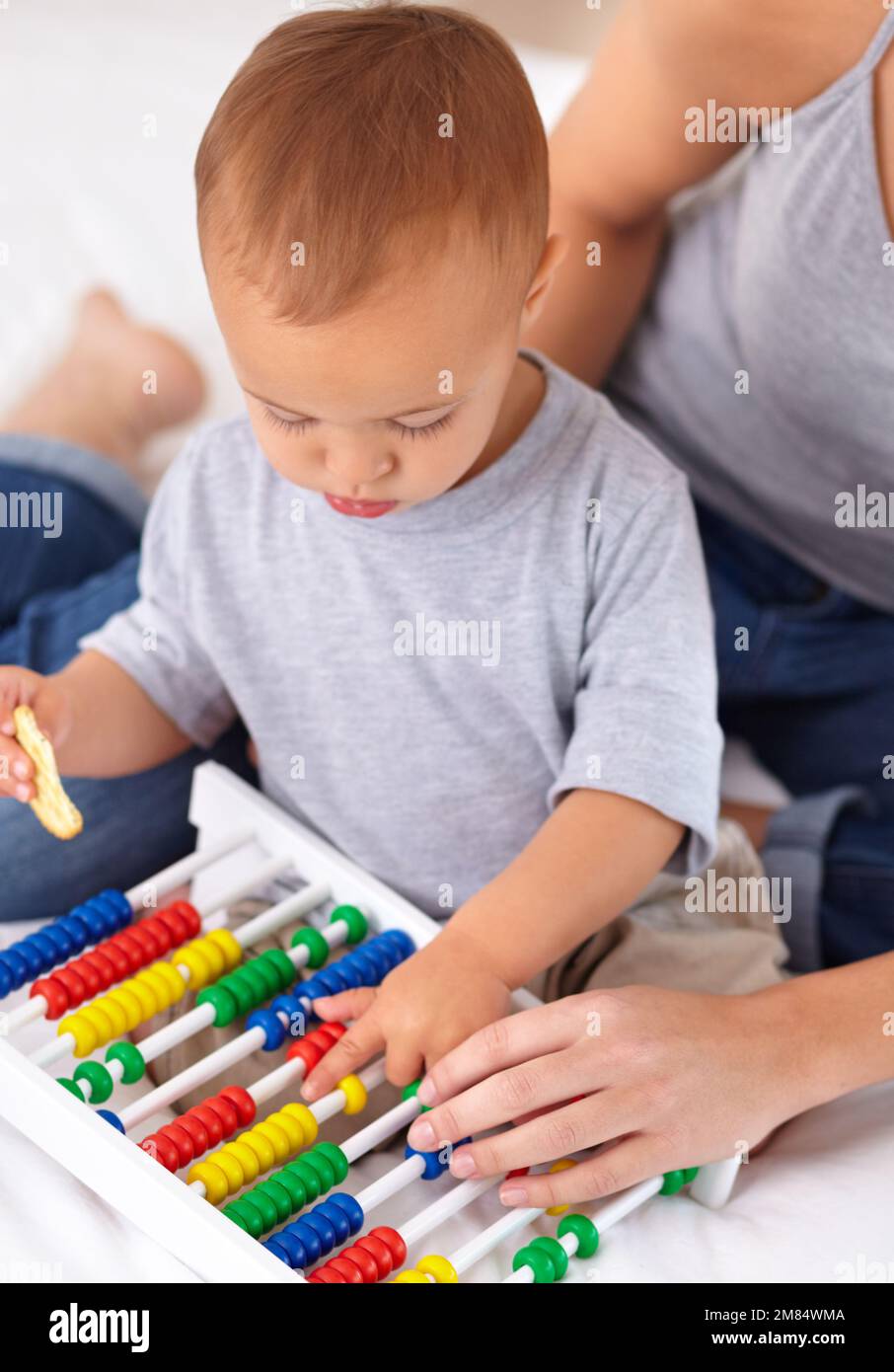 Mit Mama lernen hilft. Ein kleiner Junge, der mit einem Abakus spielt und einen Cracker isst. Stockfoto