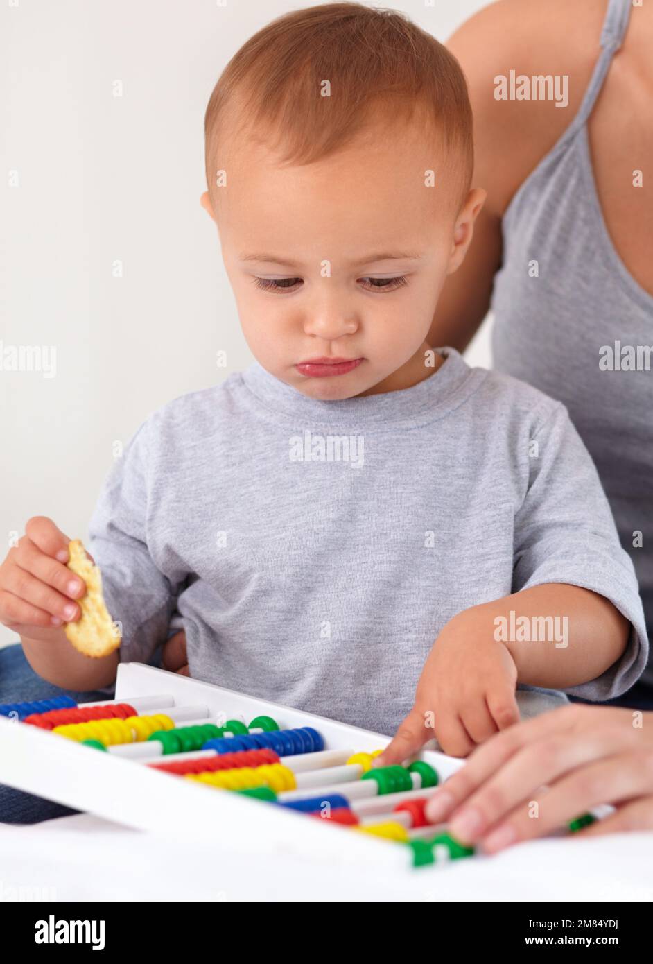 Mit Mama lernen hilft. Ein kleiner Junge, der mit einem Abakus spielt und einen Cracker isst. Stockfoto