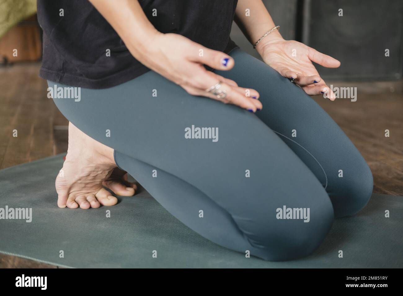 Unerkennbare Frau, die in kniender Pose meditiert, mit eingeklemmten Zehen, Hände auf Beinen, Handflächen nach oben, Yoga-Training, barfuß Stockfoto