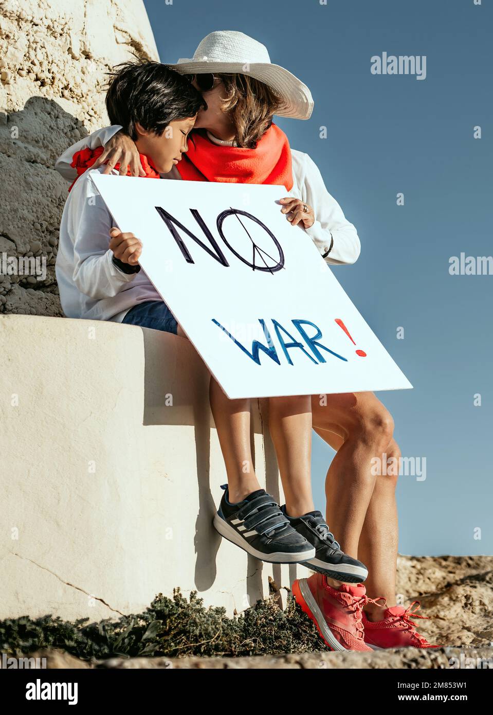 Eine Mutter tröstet ihren asiatischen Sohn vor einem Bunker und hält ein Schild mit der Aufschrift „Nein zum Krieg“. Konzeptaktivismus für den Frieden in der Welt. Stockfoto