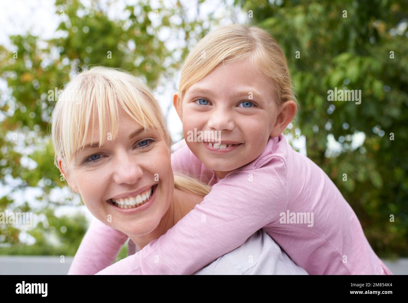 Wie die Mutter, wie die Tochter. Eine glückliche junge Mutter, die ihre Tochter im Park mit dem Huckepack fährt. Stockfoto