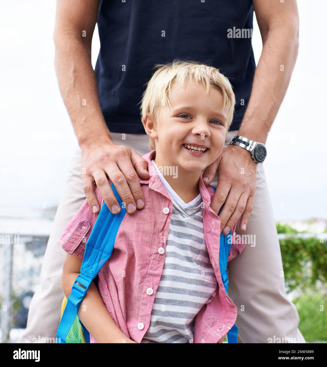 Dad wird mich vor allem beschützen. Ein kleiner Junge, der draußen lächelt, während sein Vater hinter ihm steht. Stockfoto