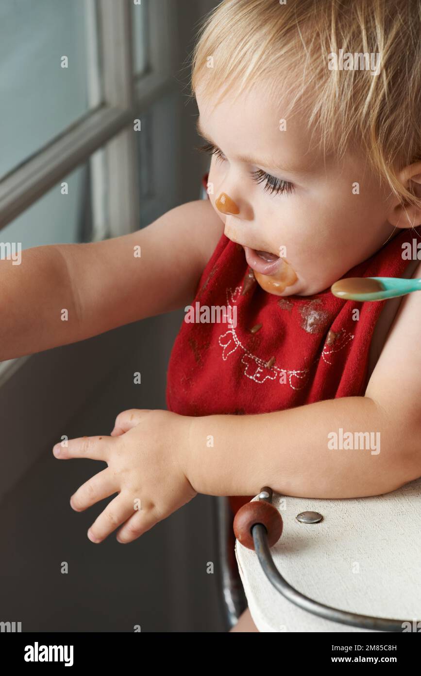 Wachsender Junge braucht sein Essen. Ein kleiner Junge, der in seinem Hochstuhl nach Herzenslust isst. Stockfoto