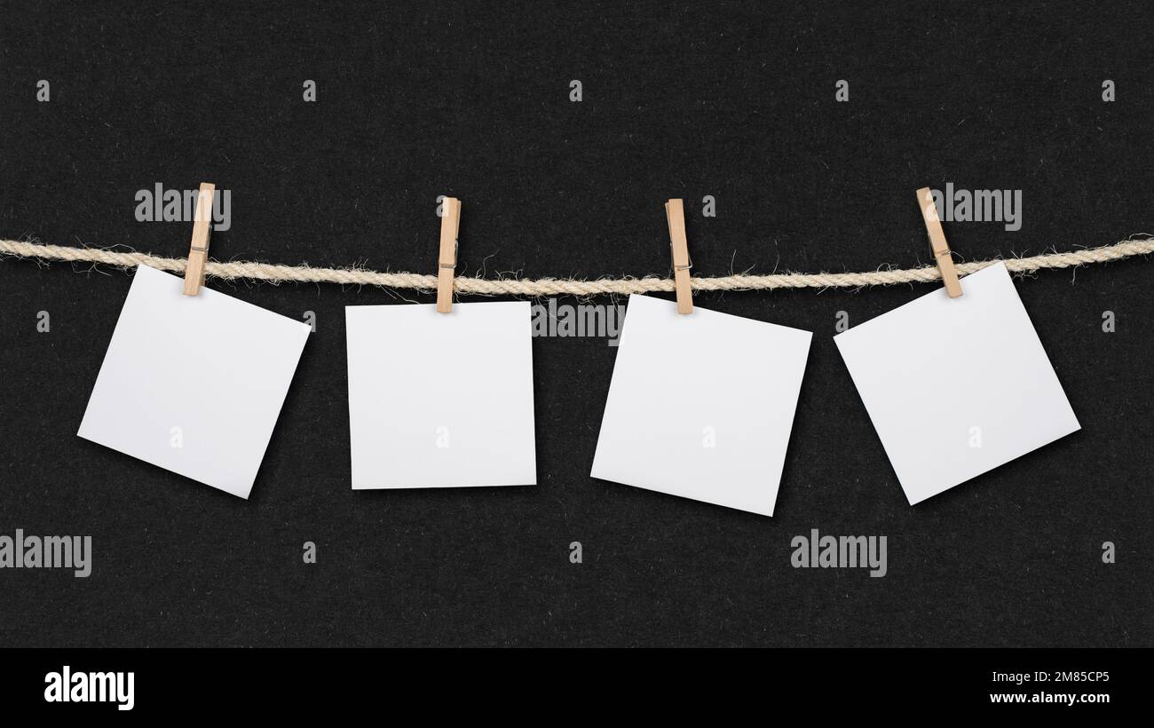 Vier leere Post-IT-Erinnerungen und Kleiderschränke, die an einem Seil auf schwarzem Retro-Papierhintergrund befestigt sind. Stockfoto