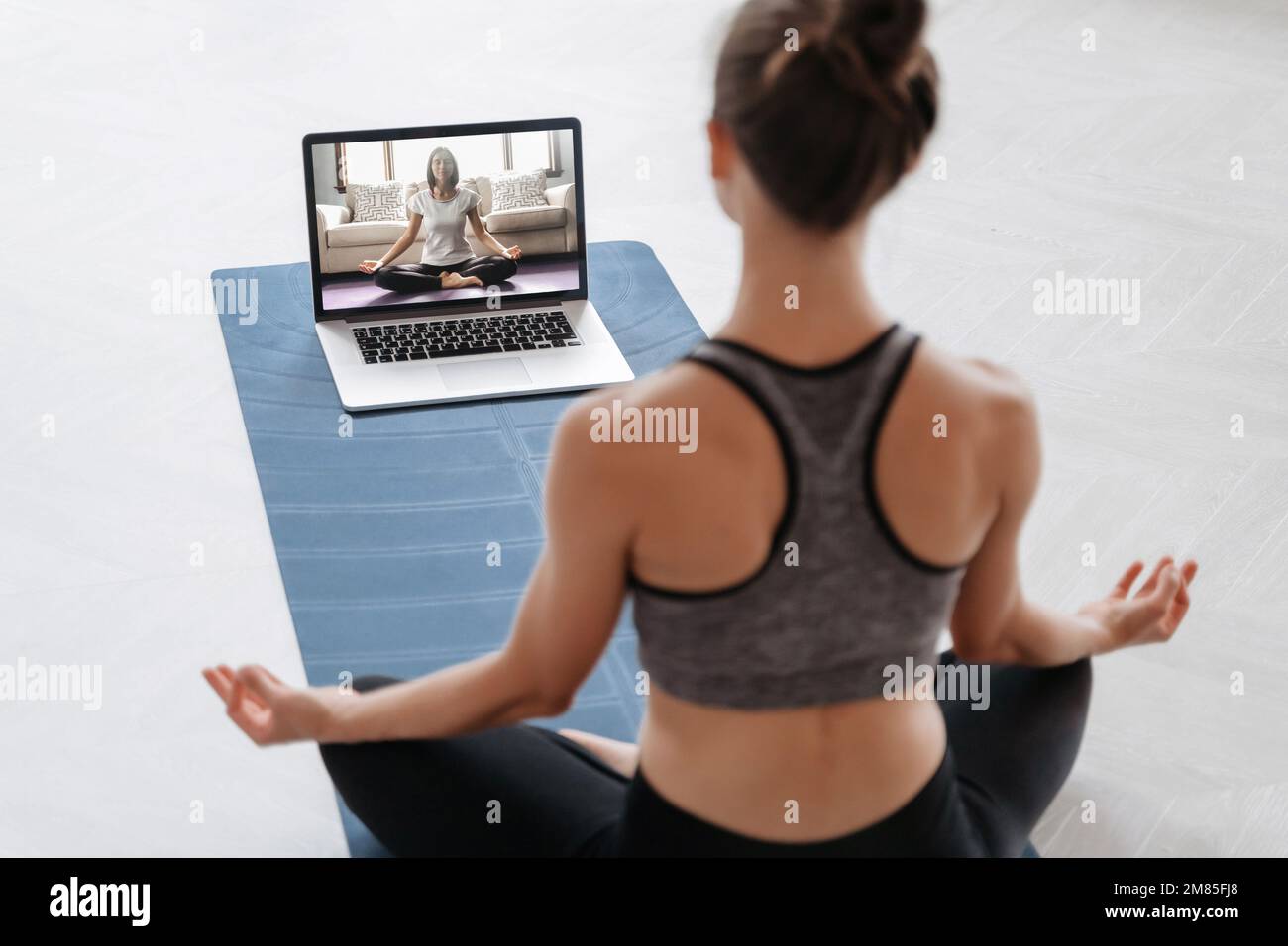 Nahaufnahme einer jungen sportlichen Frau, die online mit einem Laptop zu Hause Yoga praktiziert. Yoga-Lehrer führt Videotraining per Videokonferenz durch. Meditation, Sukhasana, entspann dich. Konzept eines gesunden Lebensstils Stockfoto