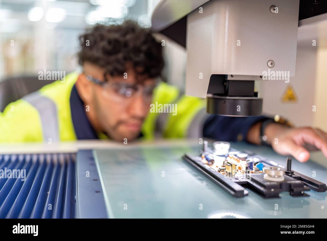 Techniker, der im Roboterherstellungsraum sitzt, verwenden das Messmikroskop, um die elektronische Platine zu prüfen Stockfoto